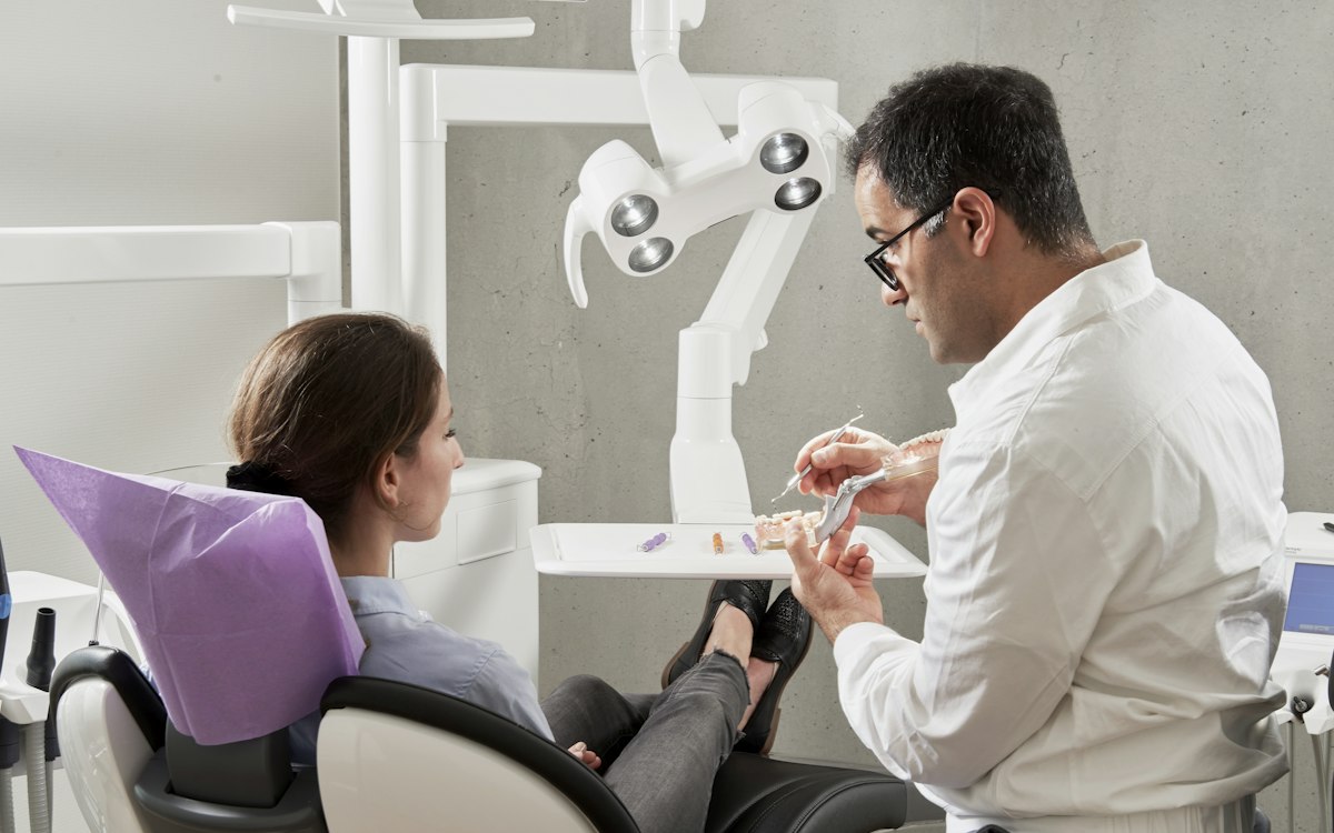 Medic stomatolog examinând o pacientă în fotoliul dentar