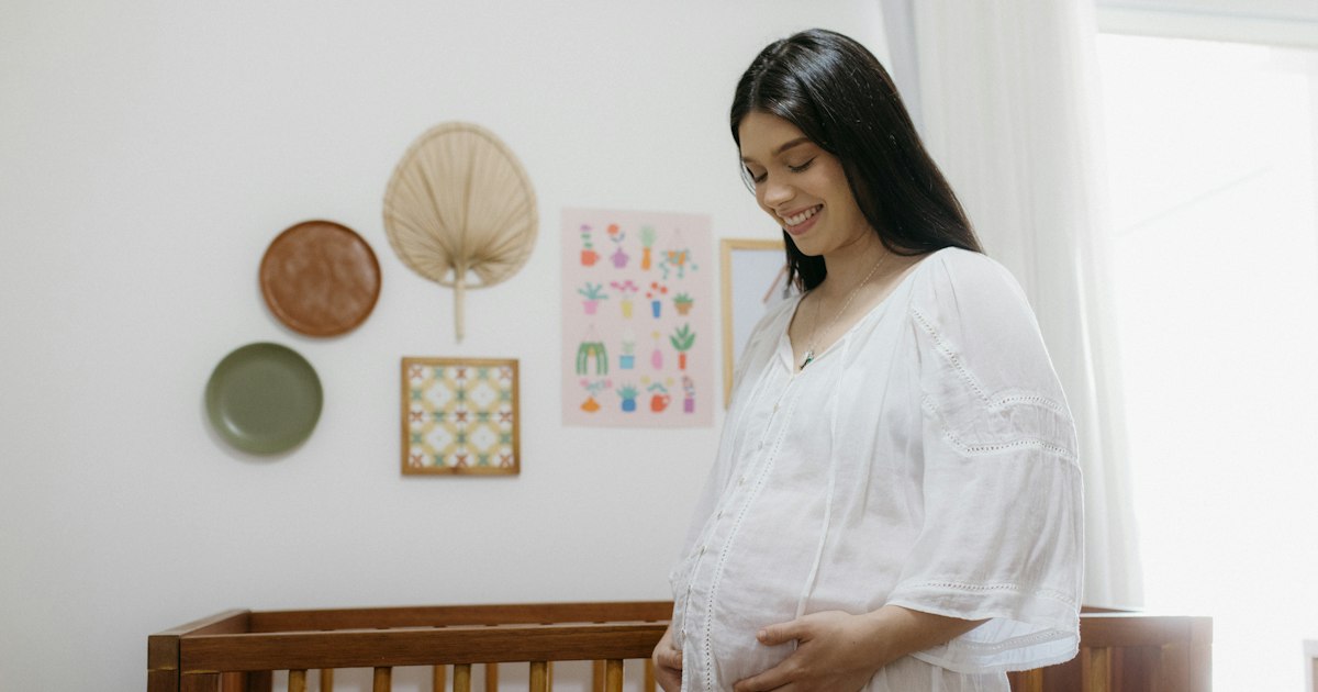 Femeie însărcinată zâmbind lângă pătuțul copilului
